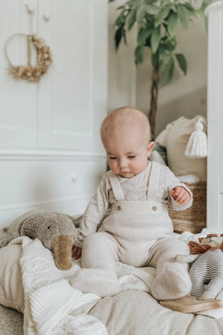 Sitting baby in nursery wearing beige knitted dungarees