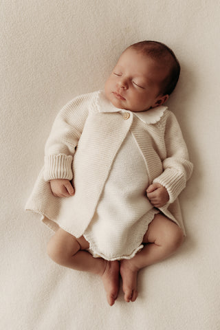 Sleeping baby wearing knitted frill collar cardigan and bodysuit
