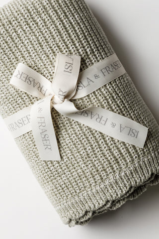Sage Green knitted baby blanket with a scalloped edge and tied with an Isla and Fraser ribbon