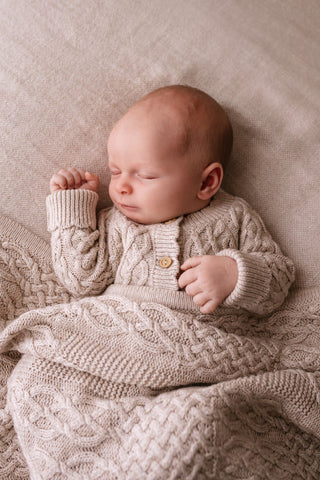 Sleeping baby wearing neutral cable knit romper with a matching blanket