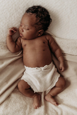 Sleeping baby lying on blankets wearing knitted bow bloomers