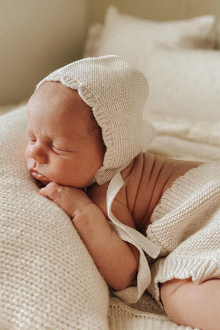 Sleeping newborn baby wearing knitted bonnet and bloomers