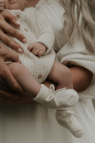 Baby being carried wearing knitted ribbed onesie and bow booties