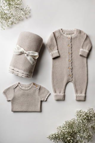 Knitted grey baby blanket tied with an Isla & Fraser ribbon, grey knitted romper, and grey folded bodysuit