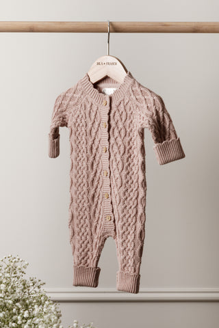 cable knit pink baby romper on wooden rail