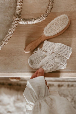 Knitted baby booties on a dresser with a hairbrush and the corner of a changing basket