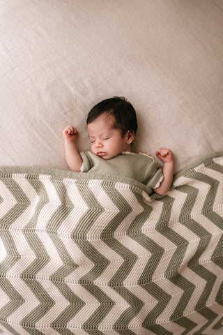 Sleeping baby wearing a sage green romper with a stripe sage and cream blanket