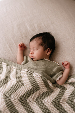 Sleeping baby wearing sage romper with a stripe sage and cream blanket
