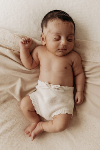 Sleeping newborn baby lying on beige blanket wearing knitted bow bloomers