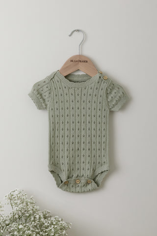 Sage green pointelle knit baby bodysuit on an Isla & Fraser wooden hanger