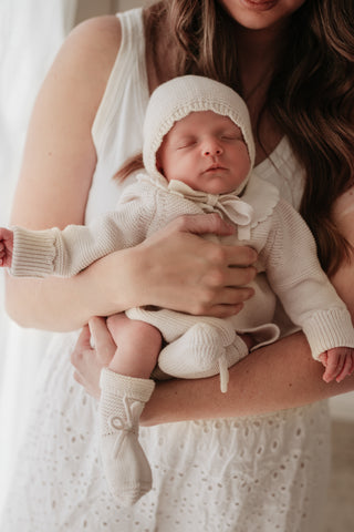 Mother carrying sleeping baby wearing a neutral knitted outfit