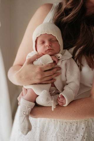 Mother carrying sleeping baby wearing a neutral knitted outfit