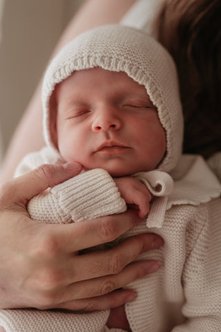 Mother carrying sleeping baby wearing a neutral knitted bonnet