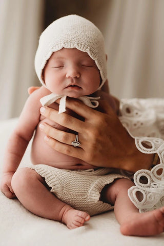 Sitting baby wearing knitted bonnet and bloomers