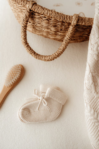Knitted bow baby booties with a baby hairbrush, moses basket, and cable knit blanket