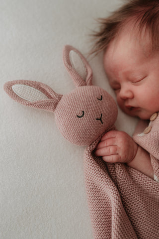 Baby holding a pink knitted bunny 