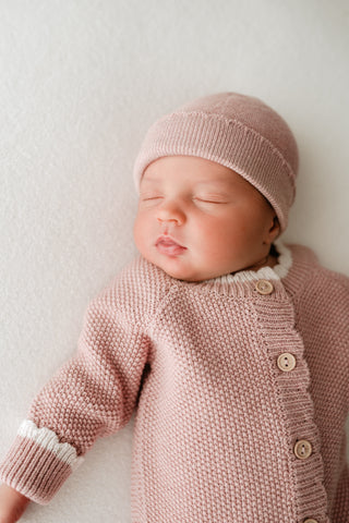 Sleeping baby wearing pink knitted hat and romper 