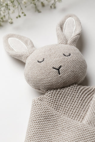 Face of a knitted bunny comforter with cream embroidered ears and dark grey embroidered face
