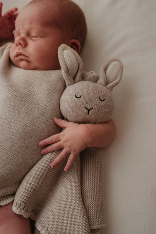 Sleeping baby cuddling a knitted grey bunny comforter
