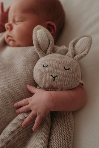 Sleeping baby cuddling a knitted grey bunny comforter