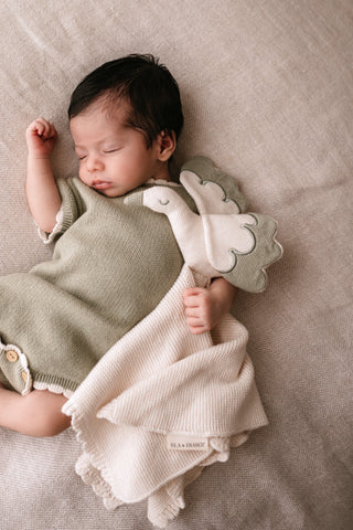 Baby cuddling a cream and sage green stork knitted comforter