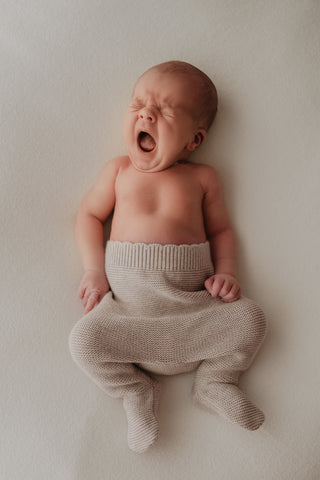 Yawning baby wearing grey knitted trousers 
