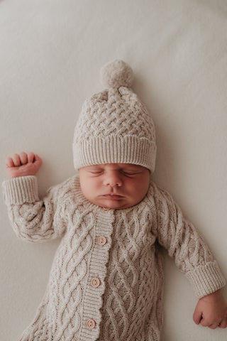 Sleeping baby wearing cable knit hat and romper
