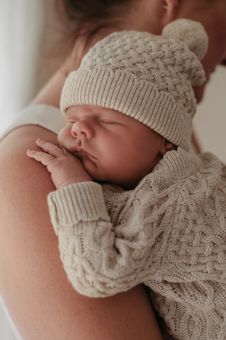 Baby sleeping on mother's shoulder wearing cable knit hat and romper
