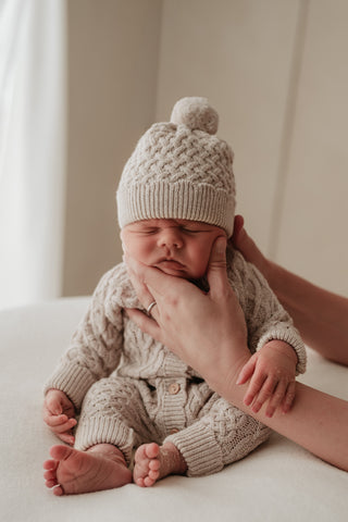 Sitting baby wearing cable knit hat and romper