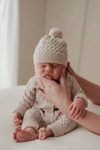 Sitting baby wearing cable knit hat and romper