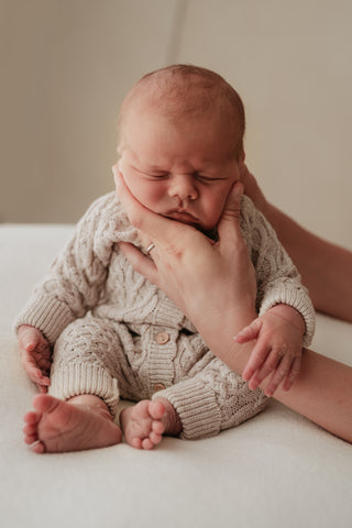 Sitting baby wearing knitted cable romper