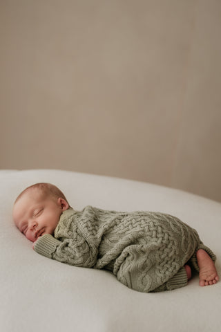 Newborn baby sleeping on their front wearing a green cable knit romper