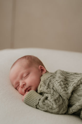 Newborn baby sleeping on their front wearing a green cable knit romper