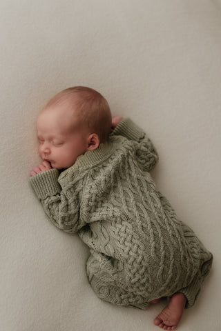 Newborn baby sleeping on their front wearing a green cable knit romper