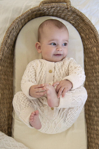 Baby in moses basket wearing beige cable knit romper
