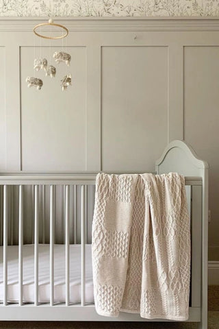 Neutral nursey with mobile, cot, and cable knit blanket