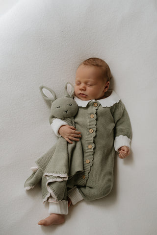 Baby wearing a sage green romper with white collar and cuffs and cuddling a sage green bunny comforter