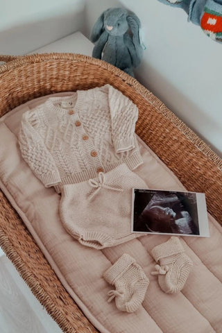 Baby Changing basket with neutral knitted cardigan, bloomers, and booties, and pregnancy scan.