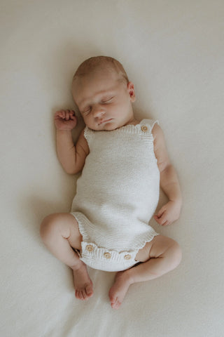 sleeping baby wearing a knitted one piece romper in beige