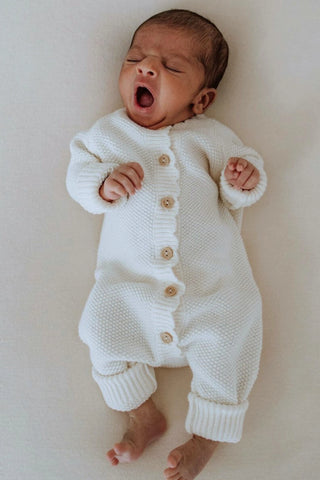 Yawning baby wearing white knitted romper