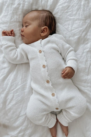 Newborn baby sleeping on white sheet wearing white knit romper