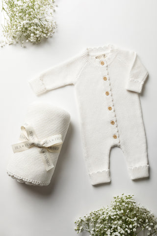 White baby blanket tied with an Isls & Fraser ribbon, and white knitted baby romper