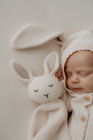 Baby wearing a cream hooded bunny outfit with a matching bunny comforter