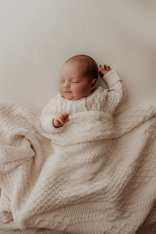 Baby wearing neutral cable knit romper and blanket