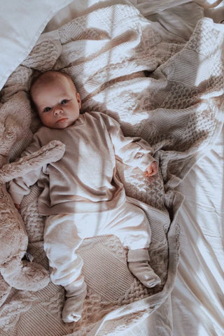 Baby in a neutral outfit lying on a cable knit blanket