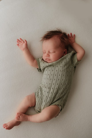 Sleeping baby wearing sage green knitted bodysuit