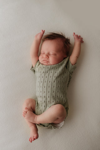 Stretching baby wearing sage green knitted bodysuit