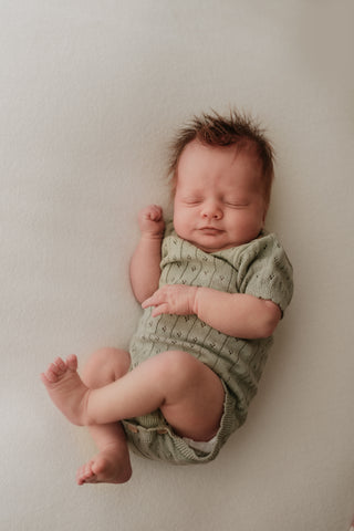 Sleeping baby wearing sage green knitted bodysuit