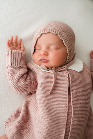 Sleeping baby wearing a pink knitted bonnet and cardigan with white collar 