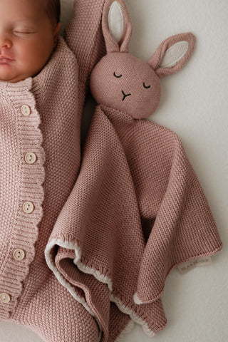 Stretching baby with a pink knitted bunny comforter 